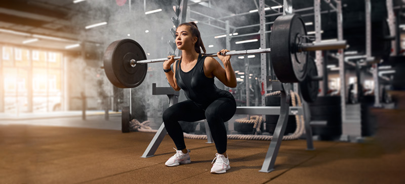 Woman lifting weight, doing squats in a gym